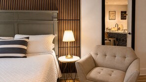 Een hotelkamer met een bed, een bedlamp, een stoel en uitzicht op de keuken.