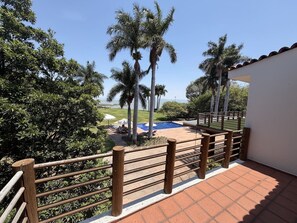 A balcony with a wooden railing overlooking a pool area with palm trees and a view of the landscape. - Chapala's Premier Lakefront Estate (Ajijic)