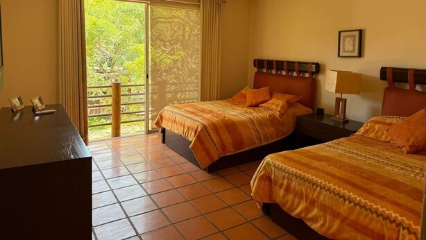 Une chambre d’hôtel avec deux lits, un bureau, un ventilateur de plafond et une vue sur la verdure par la fenêtre.
