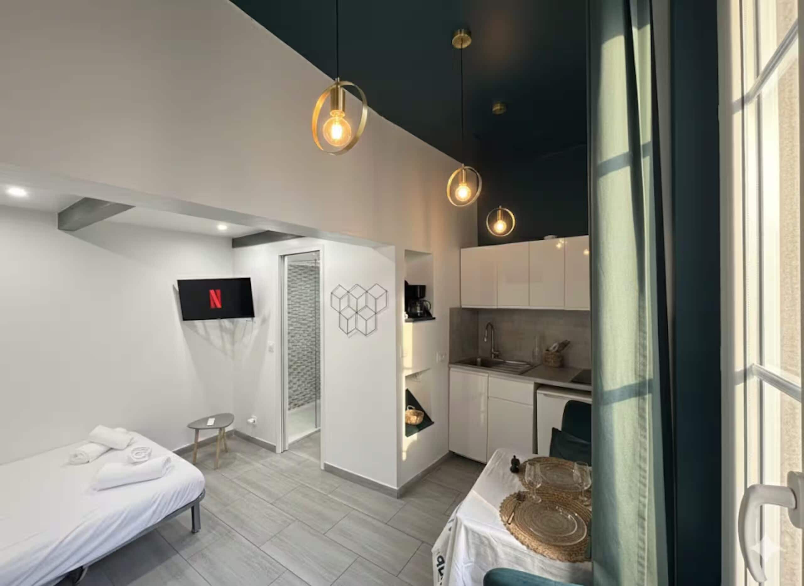 A modern hotel room with a bed, a TV, a kitchenette, and a dining area.