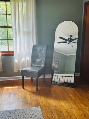 Una habitación con piso de madera, un sillón de cuero negro, un espejo grande y un ventilador de techo.