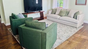Un saló amb televisió plana, butaques verdes, un sofà beix i una finestra gran amb cortines.