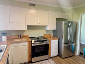 A kitchen with white cabinets, a stainless steel refrigerator, an oven, and a wooden countertop.