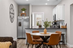 A modern kitchen with a central island, stainless steel appliances, and a dining area with orange chairs. - NEW! 6BR | 2 Condos | Sleeps 16| No Stairs (Branson)