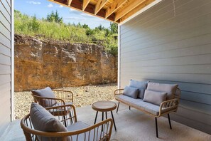 Eine Terrasse im Freien mit Korbmöbeln, einem runden Tisch und Blick auf eine natürliche Landschaft mit einer Felswand.