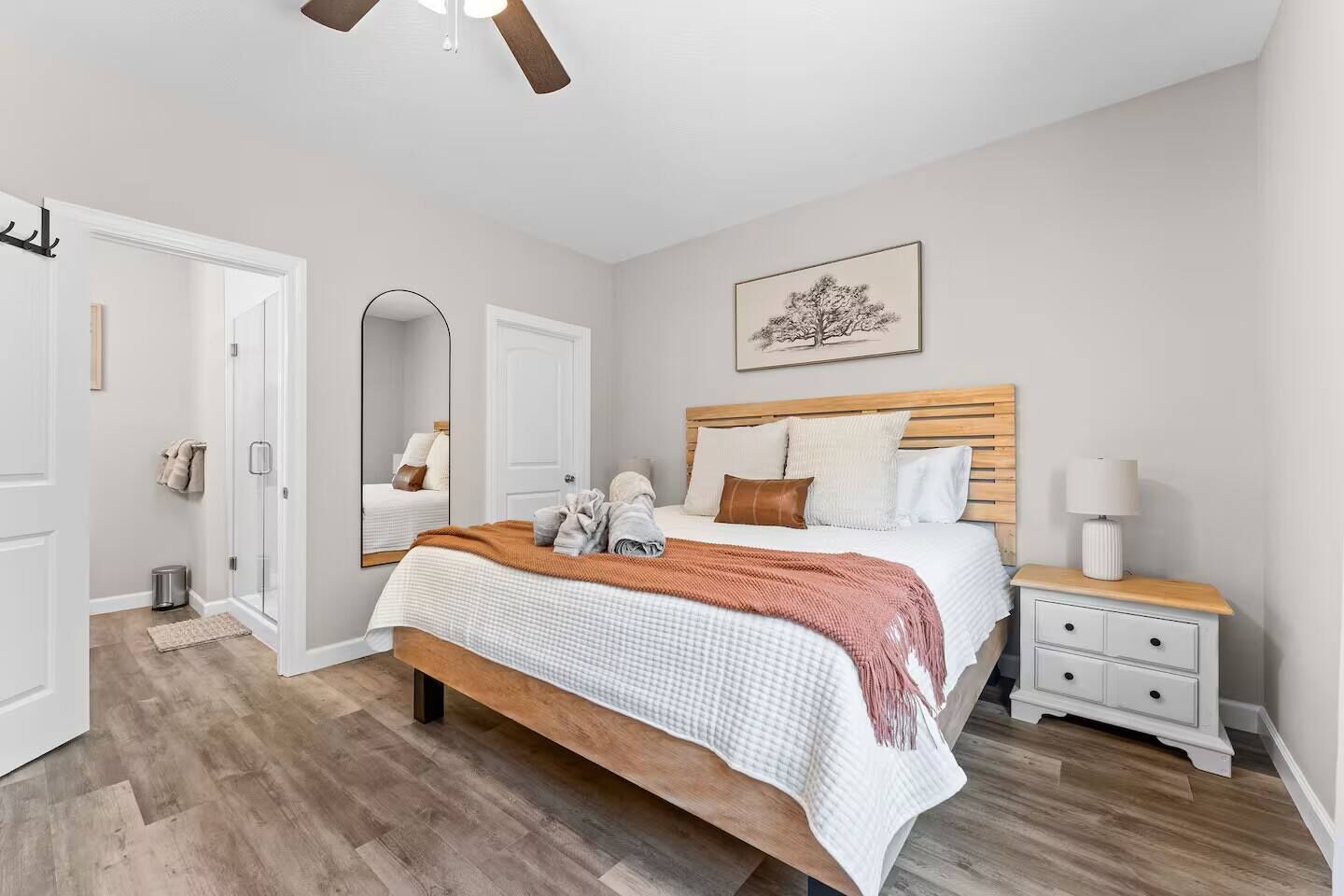 A bedroom with a bed, a nightstand, a mirror, a door, and a ceiling fan.