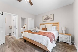 Une chambre à coucher avec un lit, une table de chevet, un miroir, une porte et un ventilateur de plafond.