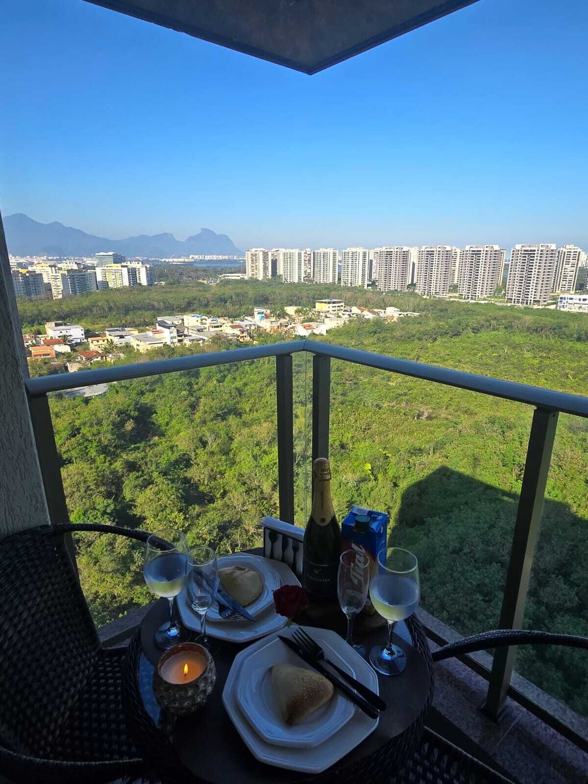A balcony with a table set for two, overlooking a cityscape with buildings and greenery.