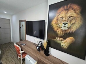 A hotel room with a large flat-screen TV mounted on the wall, a wooden desk with a chair, and a large framed picture of a lion. - Vrbo suite farmasi arena, Barra 5min, Riocentro, Rock in Rio 10min, Zona Sul 40min (Rio de Janeiro)