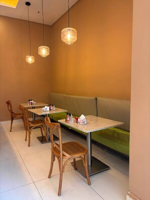 Interior de restaurante com mesas, cadeiras e um banco estofado verde.