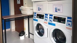 A laundry area with stacked washing machines and dryers, a table with a basket, and a door with a sign. - Vrbo suite farmasi arena, Barra 5min, Riocentro, Rock in Rio 10min, Zona Sul 40min (Rio de Janeiro)