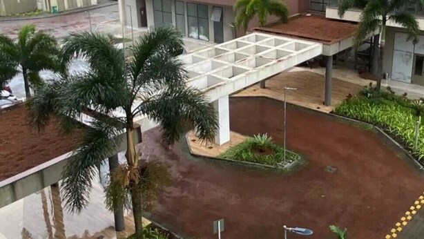 A multi-story building with a covered pedestrian walkway, palm trees, and a white car parked in the foreground. - Vrbo suite farmasi arena, Barra 5min, Riocentro, Rock in Rio 10min, Zona Sul 40min (Rio de Janeiro)