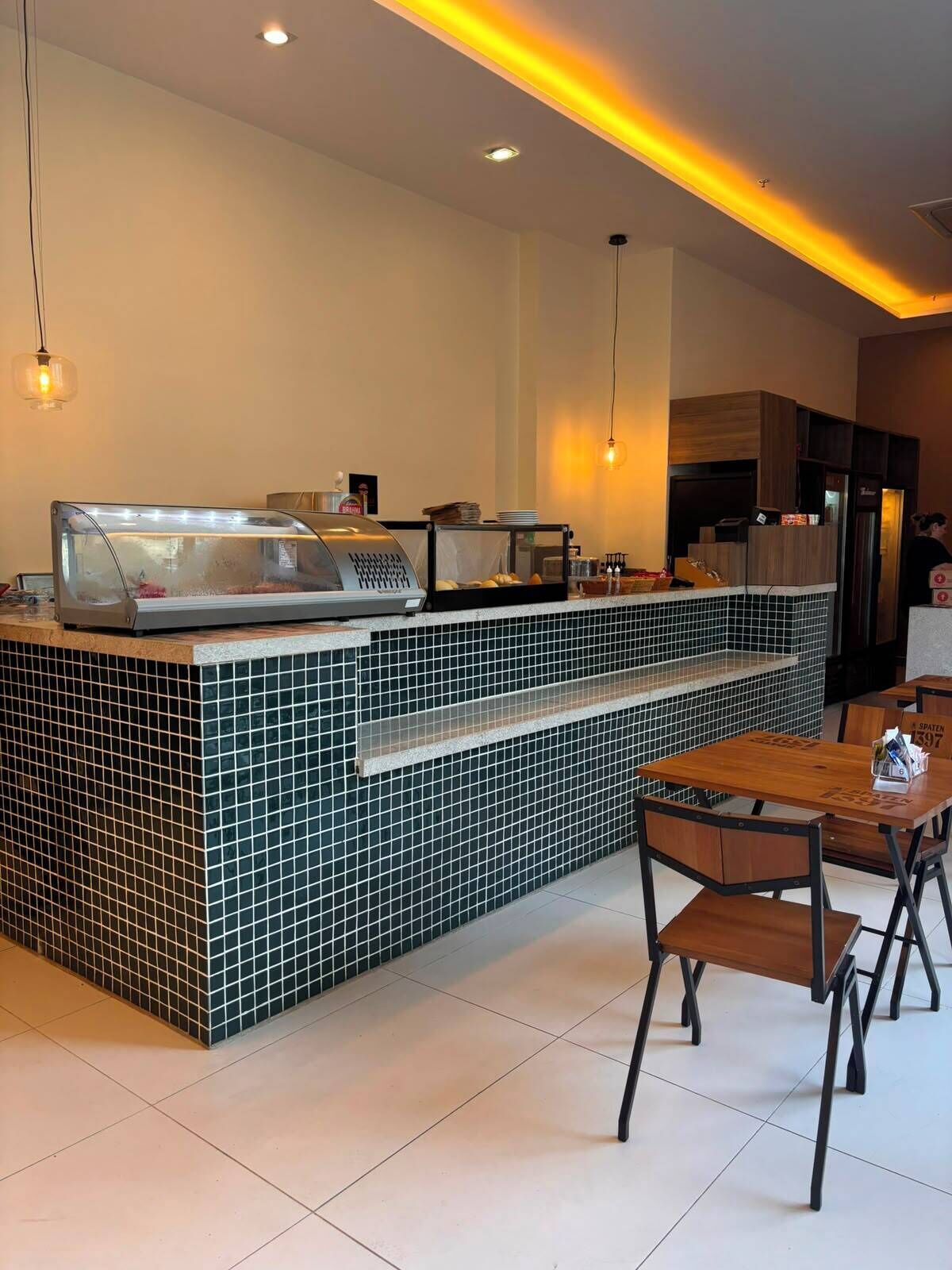 Un café moderno con mostrador de azulejos, zona de estar e iluminación colgante.