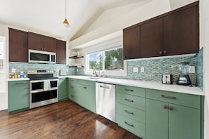 Una cucina moderna con mobili verdi, un forno a microonde, un forno e una finestra con vista sugli alberi.