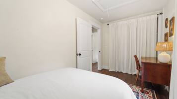 Una camera d'albergo con un letto, una scrivania, una sedia, una lampada e una porta che dà su un'altra stanza.