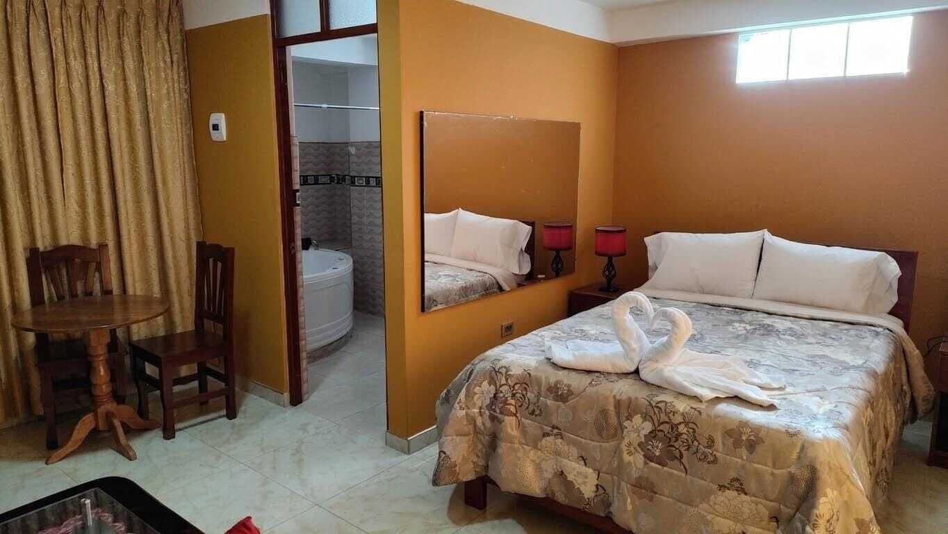 Habitación de hotel con cama, una silla, una mesa, un espejo y un baño visible a través de una puerta abierta.