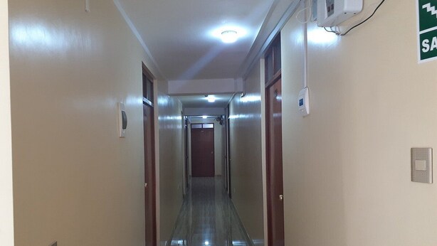 A long, narrow hallway with doors on either side, a light fixture on the ceiling, and a fire alarm on the wall.