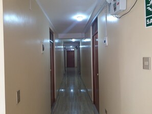 A long, narrow hallway with doors on either side, a light fixture on the ceiling, and a fire alarm on the wall. - HOTEL EL CASTOR HUARAZ (Huaraz)