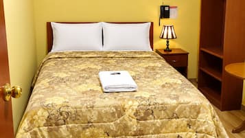 A bed with a floral bedspread, a bedside lamp, a wooden wardrobe, and a door with a golden handle.
