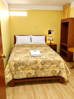 A bed with a floral bedspread, a bedside lamp, a wooden wardrobe, and a door with a golden handle. - HOTEL EL CASTOR HUARAZ (Huaraz)