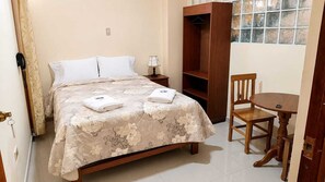 Un dormitorio con cama, mesita de noche, armario de madera, una silla y una pequeña mesa.