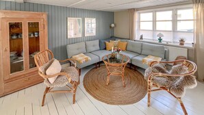 Ein Zimmer mit einem hellblauen Sofa, Korbstühlen, einem Glastisch und einer Holzkabine mit Glastüren.