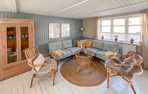 A room with a light blue sofa, wicker chairs, a glass coffee table, and a wooden cabinet with glass doors. - Awesome home in Sæby with WiFi (Sæby)