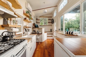 A modern kitchen with wooden shelves, a stove, and a large window overlooking greenery. - Topanga Canyon Oasis - 3 Homes & Pool - C&C | 12 (Topanga)