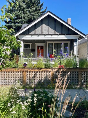 Ein zweistöckiges Haus mit Veranda, Holzzaun und verschiedenen Pflanzen und Blumen.
