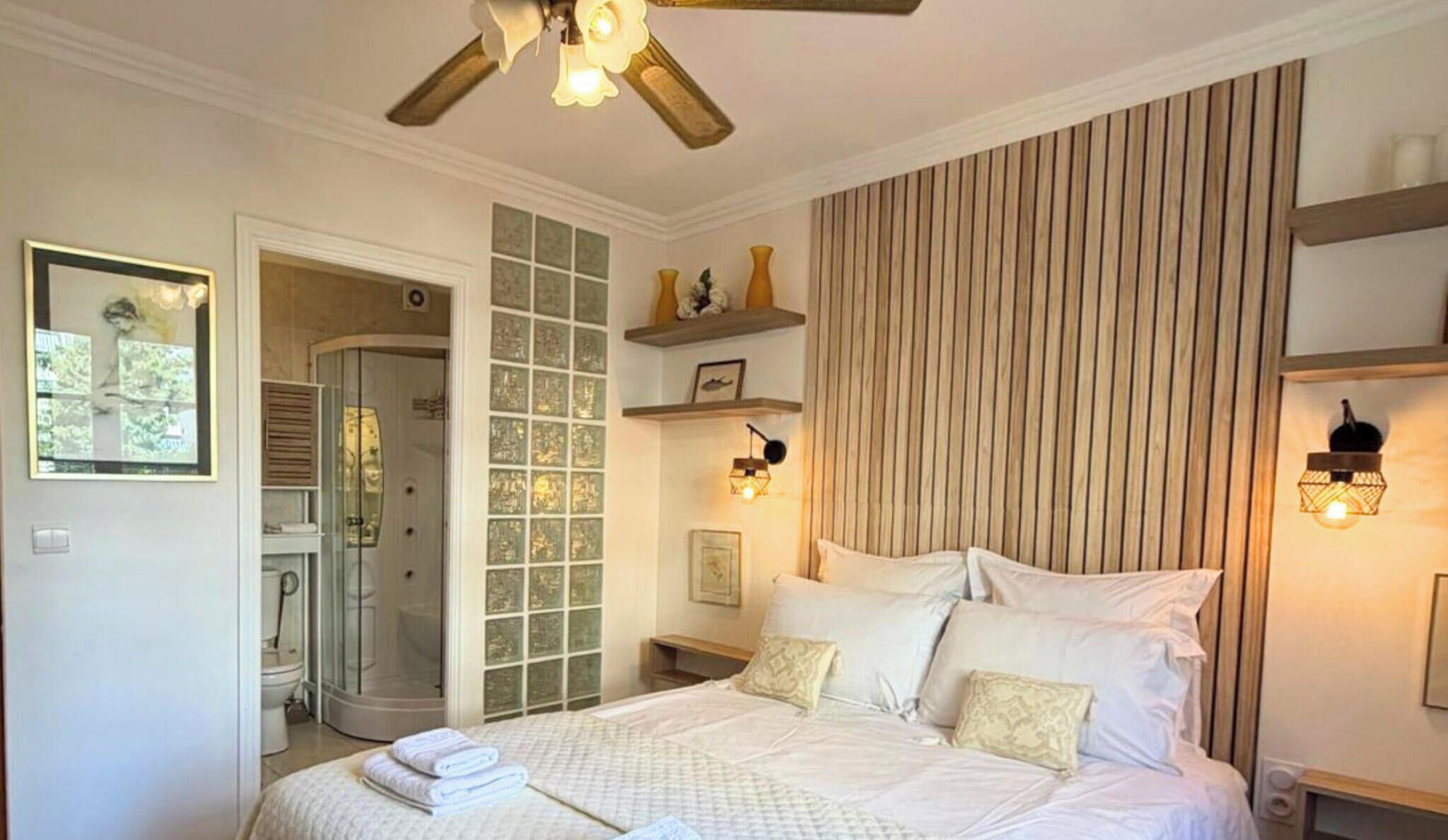 Een slaapkamer met een bed, een douche, een deur naar een badkamer en een muur met een verticaal patroon.