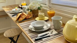 Ein Frühstückstisch mit Croissants, Orangensaft und Blumen am Fenster.