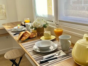Ein Frühstückstisch mit Croissants, Orangensaft und Blumen am Fenster.