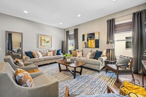 A modern living room with a sectional sofa, a coffee table, and a dining area with a small table and chairs. - Lux Home Close to Broadway • Rooftop Views & FirePit! (Nashville)