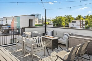A rooftop terrace with outdoor furniture, a fire pit, and a view of the cityscape. - Lux Home Close to Broadway • Rooftop Views & FirePit! (Nashville)