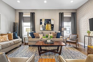 A modern living room with a sofa set, a coffee table, and a large abstract painting on the wall. - Lux Home Close to Broadway • Rooftop Views & FirePit! (Nashville)