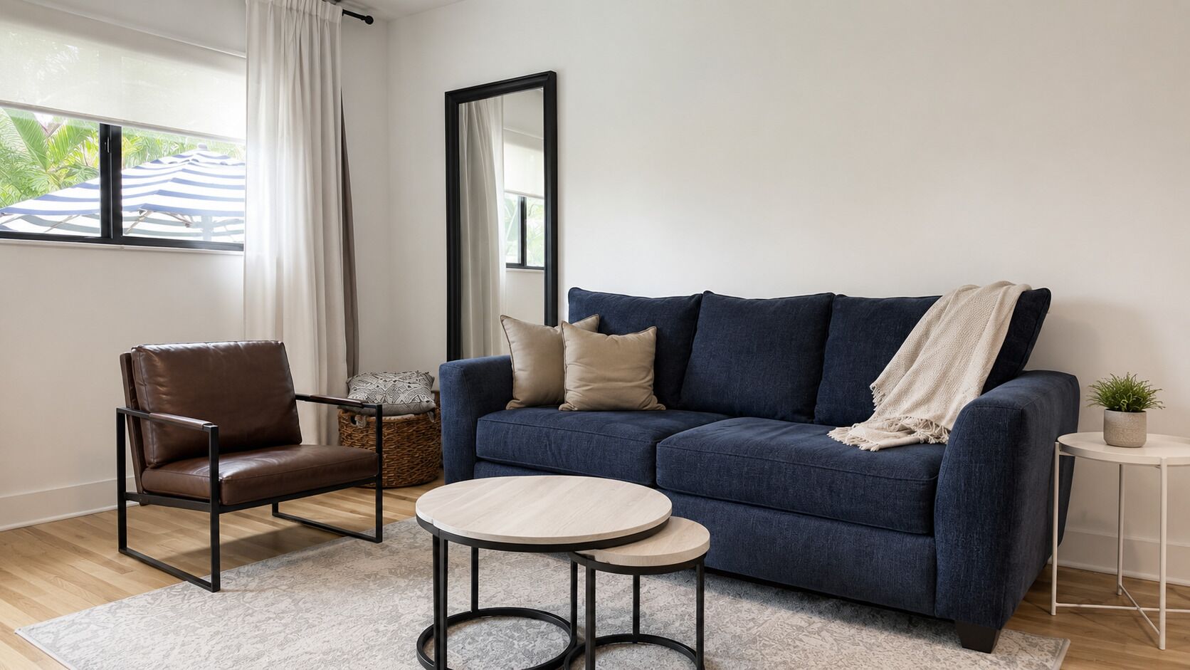 A living room with a sofa, a chair, a small table, a mirror, and a potted plant.