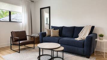 A living room with a sofa, a chair, a small table, a mirror, and a potted plant.