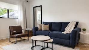 Ein Wohnzimmer mit einer Couch, einem Sessel, einem kleinen Tisch, einem Spiegel und einer Topfpflanze.