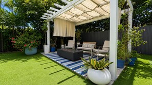 Ein überdachter Patio-Bereich mit Sitzgelegenheiten, Kunstrasen und Topfpflanzen.
