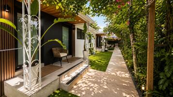 A modern outdoor seating area with a chair and a table, a pathway leading to a building, and lush greenery.
