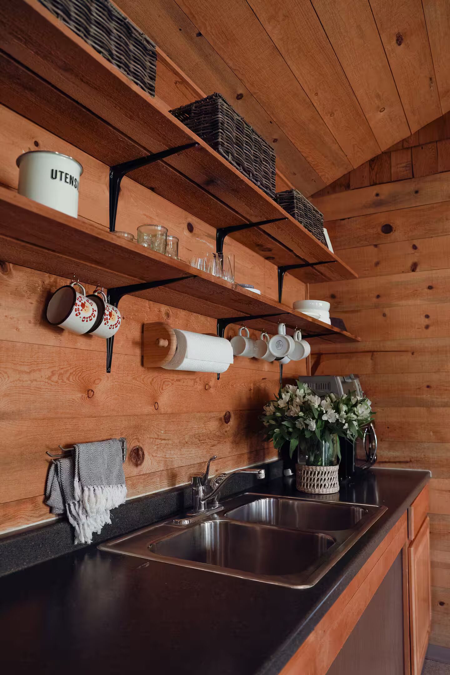 A kitchen with wooden shelves, hanging mugs, and a sink.