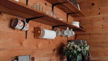 A kitchen with wooden shelves, hanging mugs, and a sink.