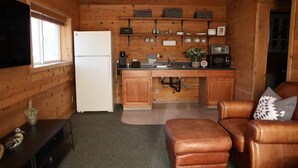 Eine kompakte Küche mit Kühlschrank, Spüle und Mikrowelle. Es gibt eine Sitzecke mit einer Ledersofa und einem kleinen Tisch.