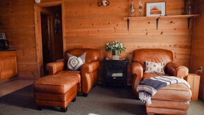 Ein gemütliches Blockhaus-Interieur mit Ledersofas, einem Kamin und einem kleinen Tisch mit einer Blumenvase.