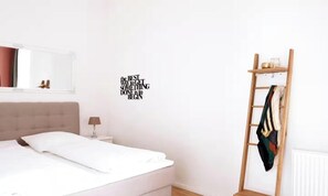 A bedroom with a bed, a nightstand, a lamp, a ladder, and a motivational wall decal. - AN EXCELLENT COMBINATION OF MODERN AMENITIES, GENEROUS LIVING SPACE IN THE HEART (Berlin)