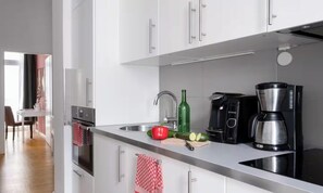 A modern kitchen with white cabinets, stainless steel appliances, and a countertop with a coffee maker, a bottle, and a red bell pepper. - AN EXCELLENT COMBINATION OF MODERN AMENITIES, GENEROUS LIVING SPACE IN THE HEART (Berlin)