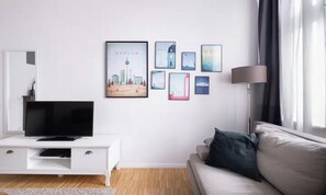 A modern living room with a flat-screen TV on a white cabinet, a sofa with a dark cushion, and a series of framed pictures on the wall. - AN EXCELLENT COMBINATION OF MODERN AMENITIES, GENEROUS LIVING SPACE IN THE HEART (Berlin)