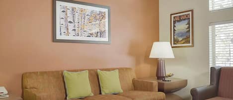 Een woonkamer met een bank, een lamp en twee afbeeldingen in lijsten aan de muur.