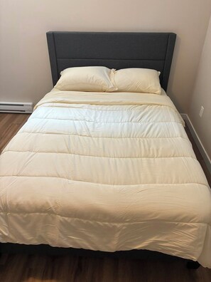 Ein Bett mit dunklem Kopfteil und cremefarbener Bettdecke.