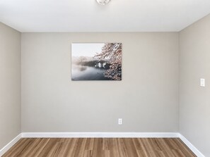 Ein Zimmer mit Holzboden, einer schlichten Wand und einem einzelnen gerahmten Bild.